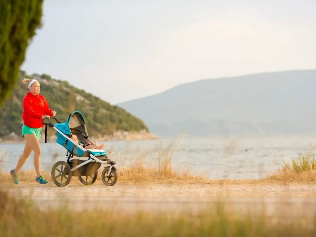 Mummy jogging with a baby on an all terrain stroller in a field beside the sea