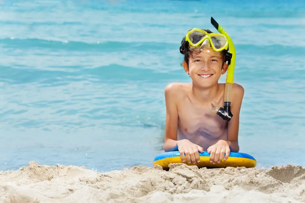 boy with snorkel set sitting in the ocean