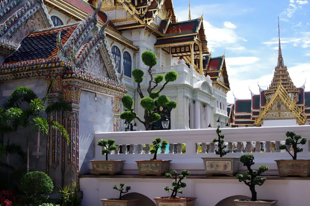 A close-up of Thai temples of the Bangkok Royal Palace featuring white and golden colors and some green plants, one of the top things to do in Bangkok for families