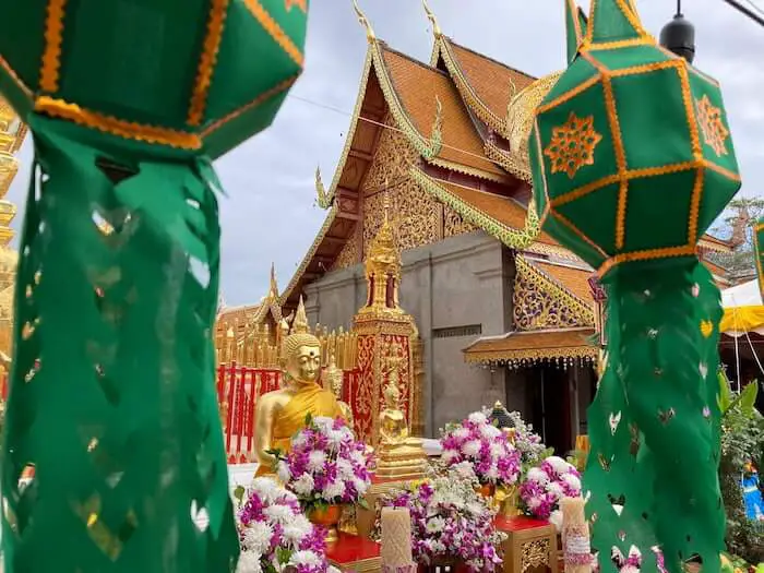 Golden buddha with flowers in front of a temple in between green pillars at doi sethup, Chiang Mai, in daytime