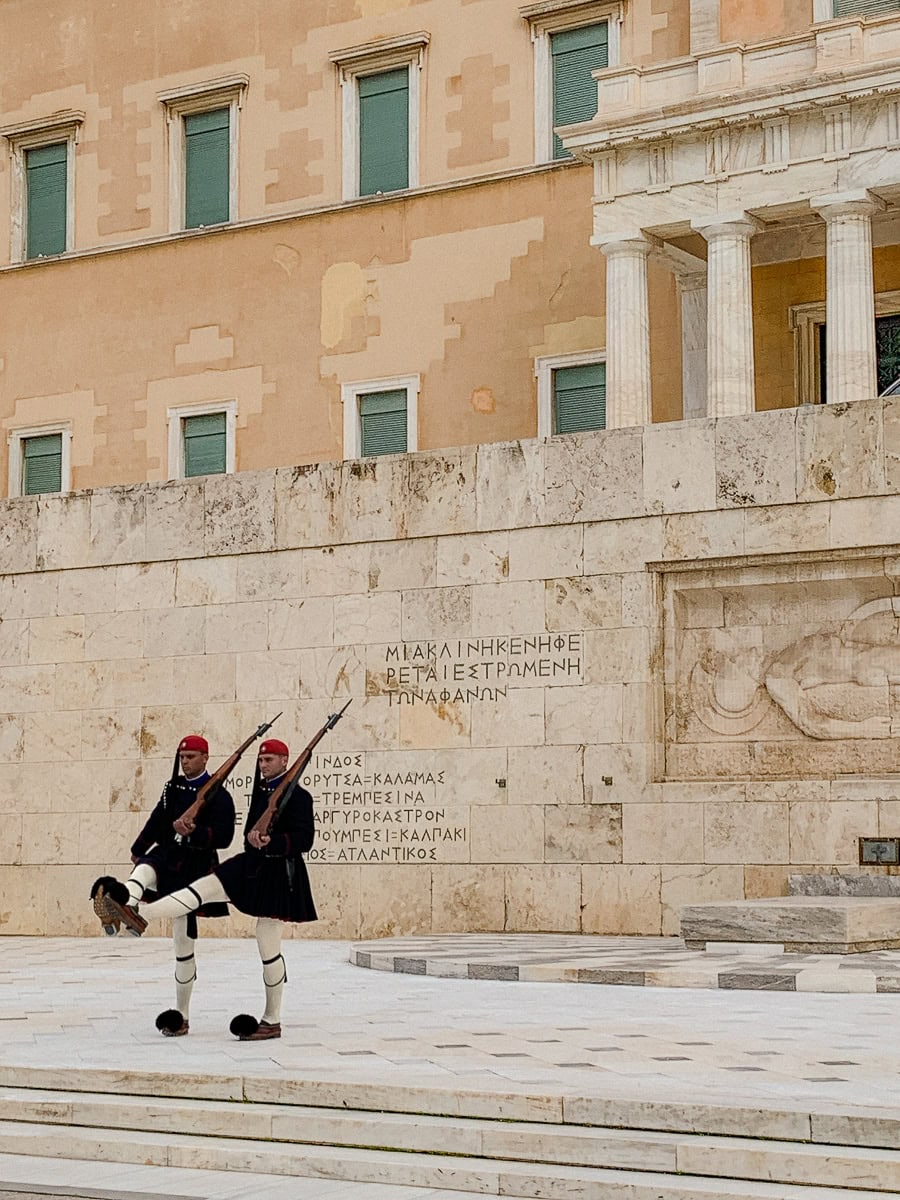 2 evzones raising their leg in front of the monument of the unknown soldier.