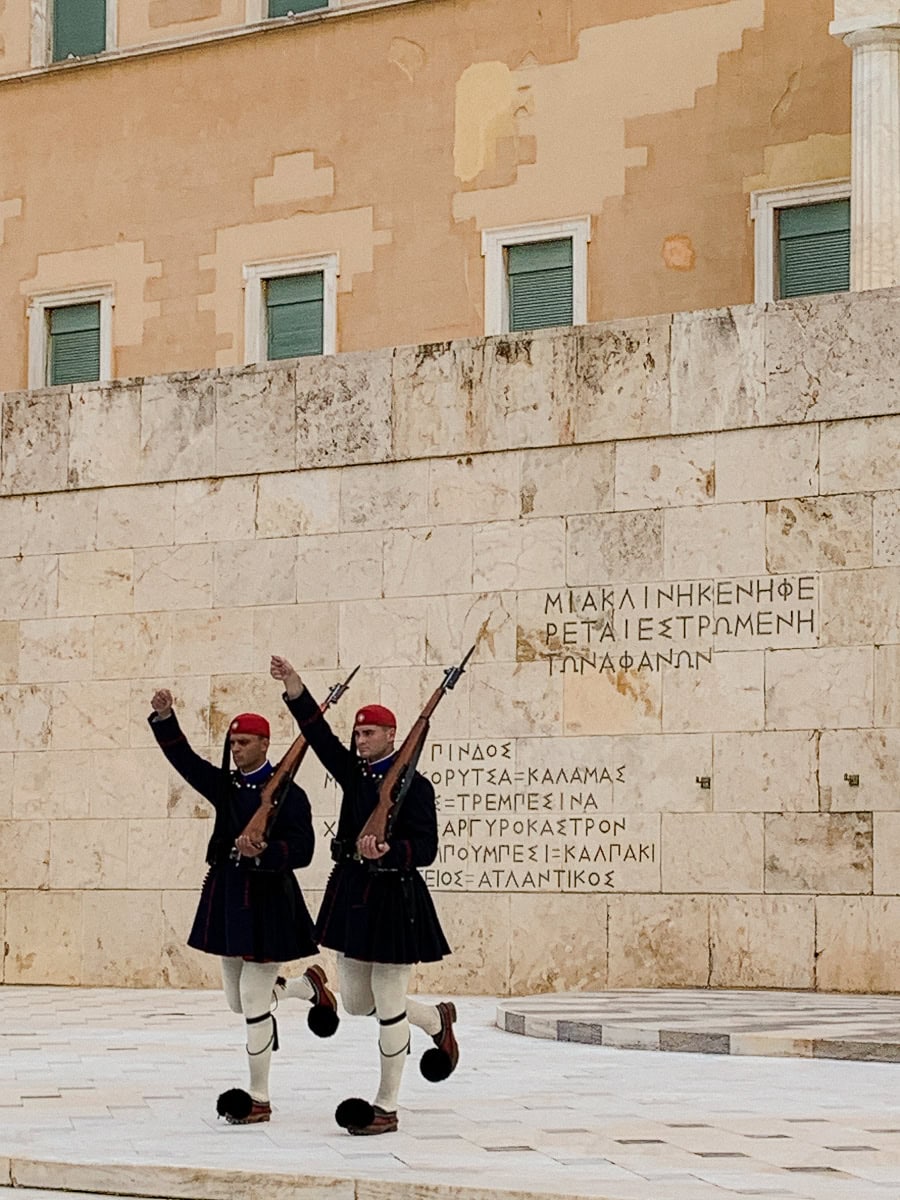 2 evzones raising their hands in front of the monument of the unknown soldier.