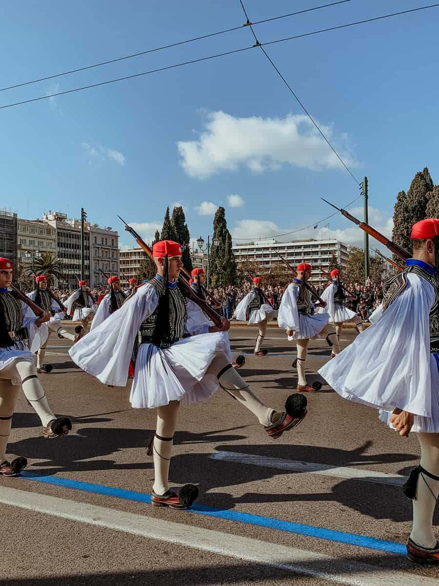 Evzones marching by in their traditional outfits.