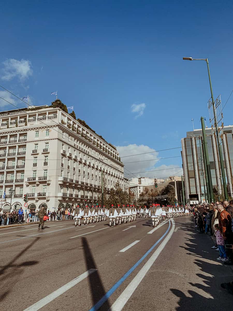 Evzones marching away on the street in their white outfits.