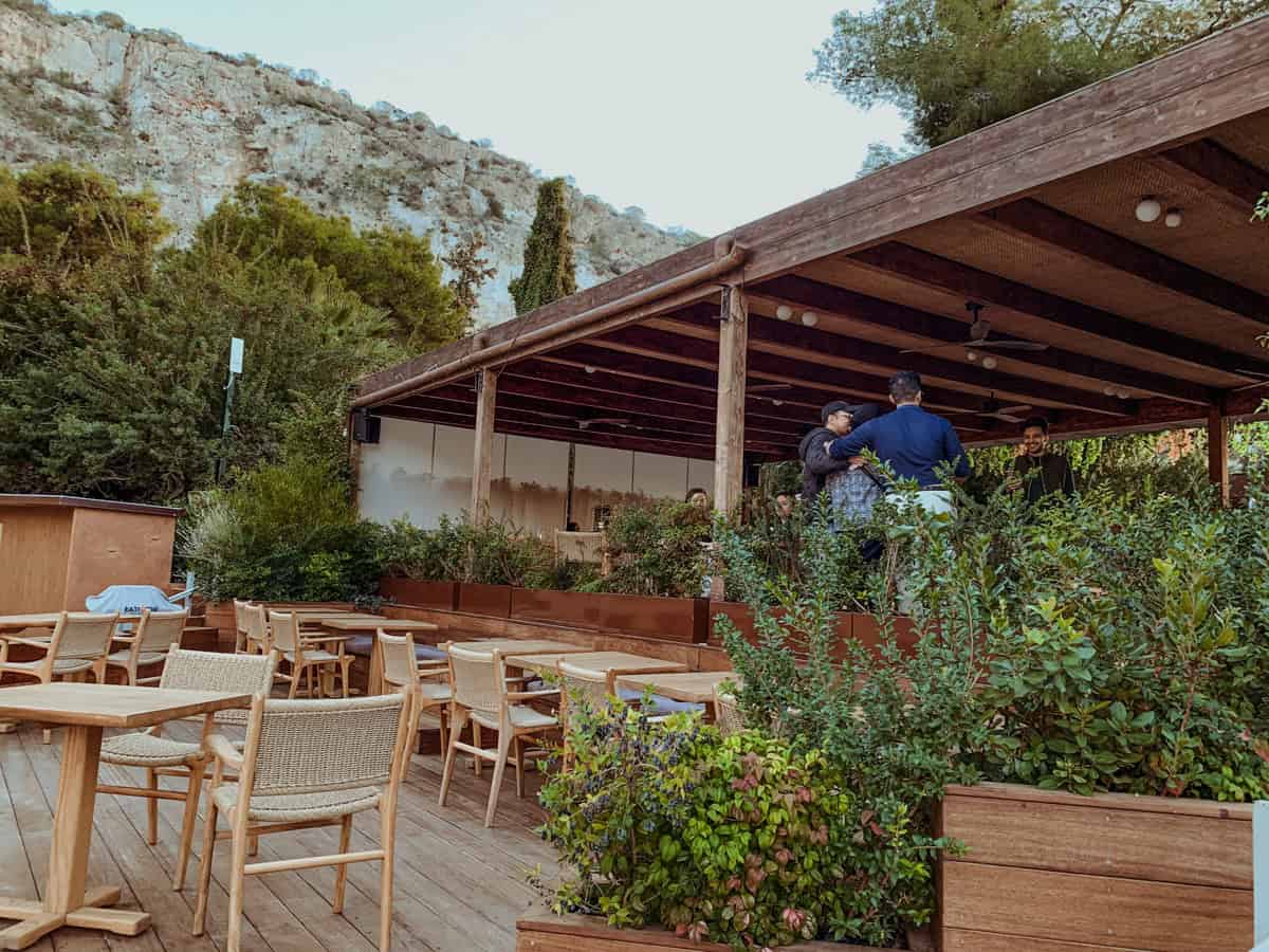 Restaurant in Lake Vouliagmeni with chairs and umbrellas. With a small area that has a roof and with a beautiful view of the rocky mountains nearby.