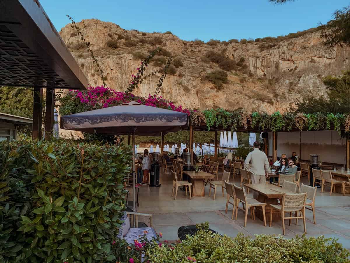 Restaurant in Lake Vouliagmeni with chairs and umbrellas with a beautiful view of the rocky mountains nearby.