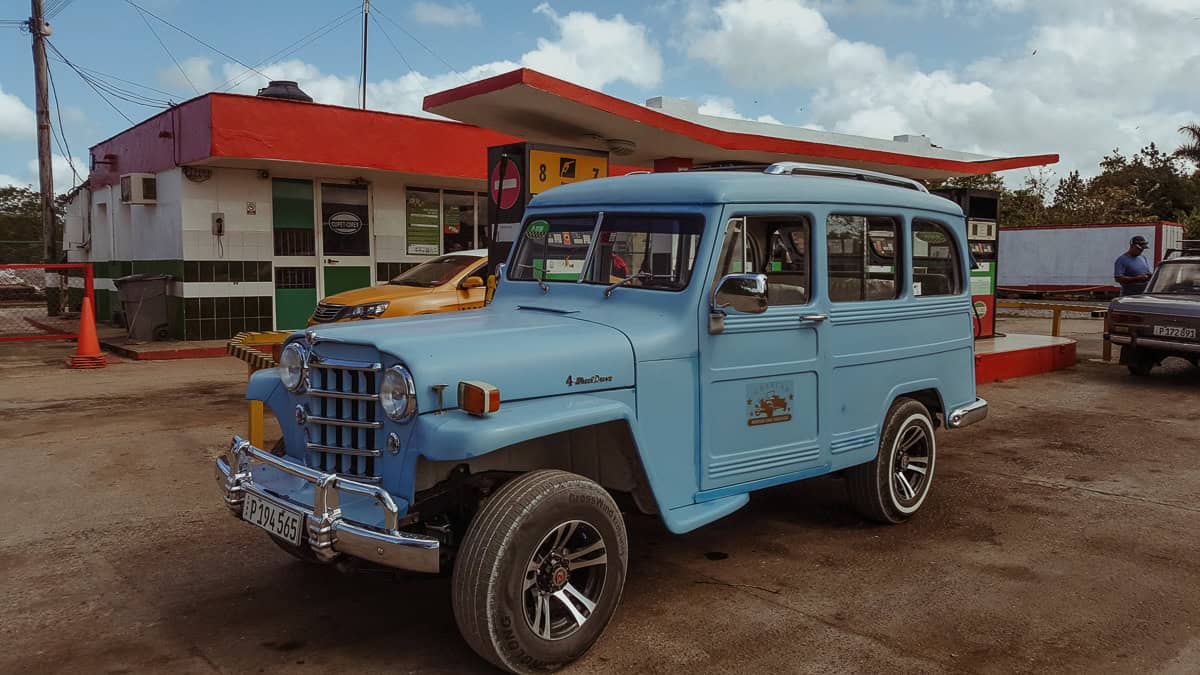 A light blue vintage Willys Jeep Station Wagon at a gas station in Cuba.