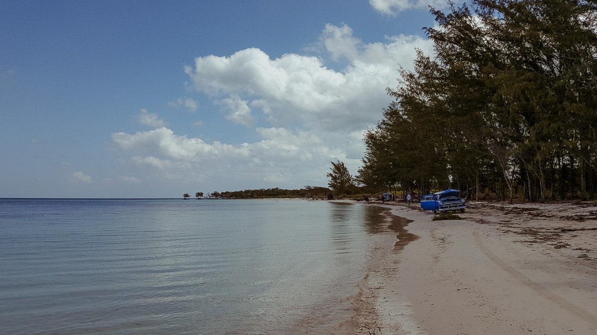 Scenic beach view with a blue Jeep parked on the sandy shore.