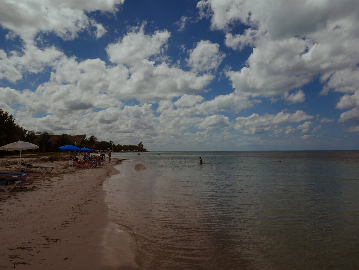 Scenic beach with a tourist lounging on the sandy shore under a partly cloudy sky.