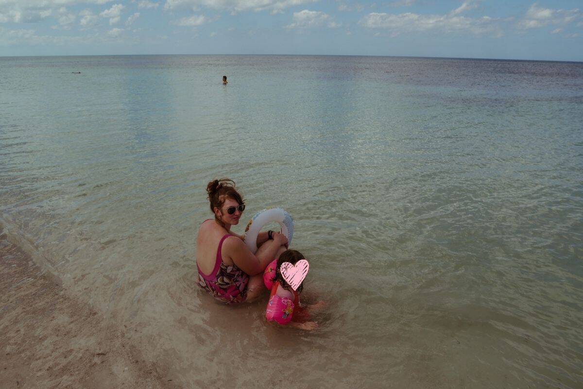 Babs and our daughter Norah are sitting in the shallow water near the shore.