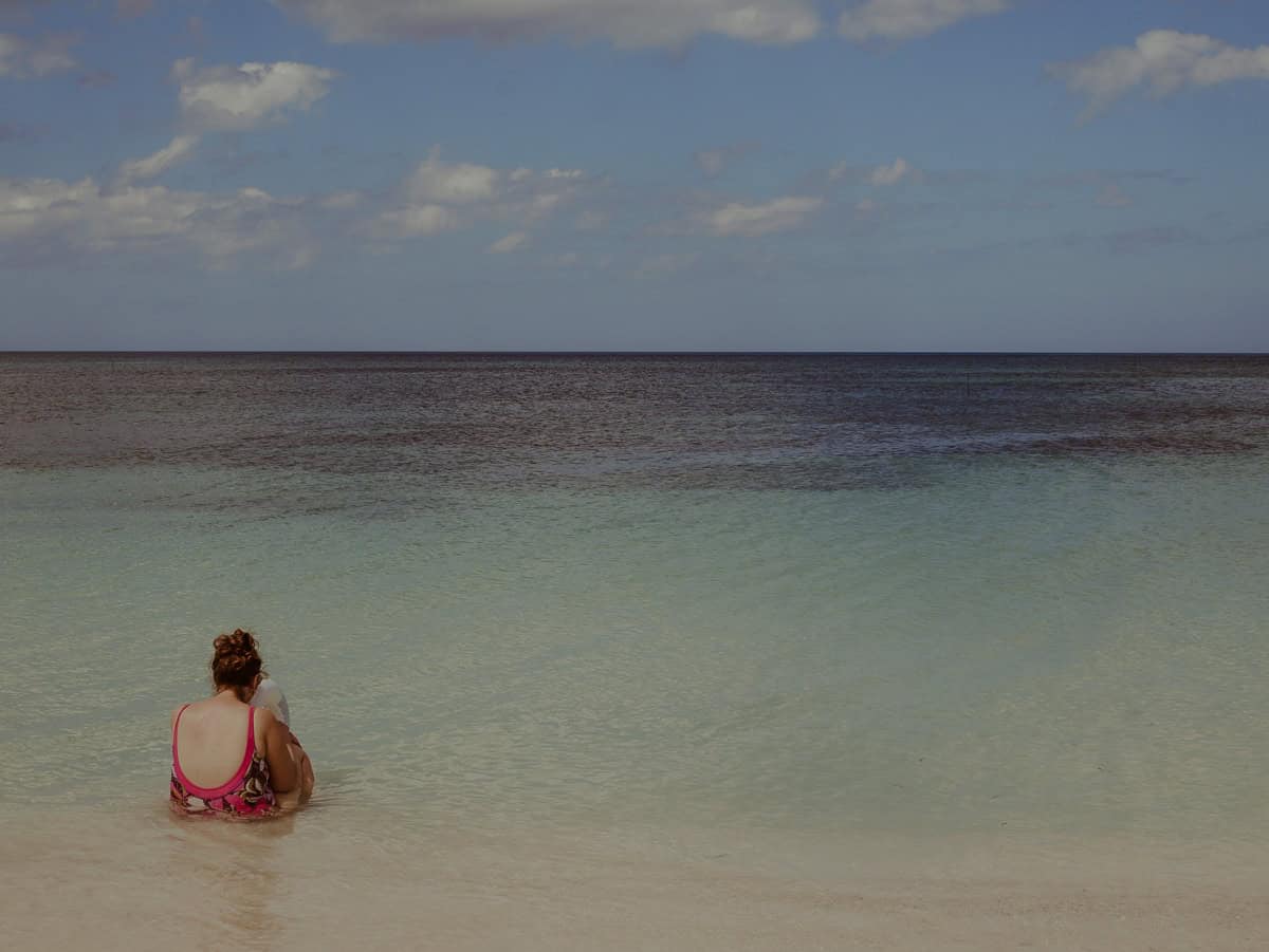 Babs is sitting in the shallow water near the shore, facing the ocean.