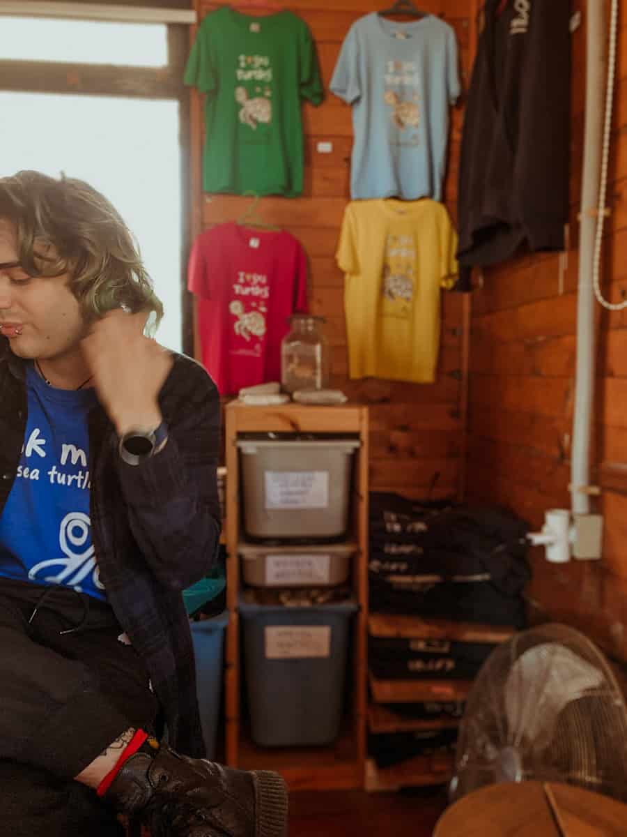 Our guide sits in a wood-panelled gift shop, with colourful 'I Love Turtles' t-shirts displayed behind.