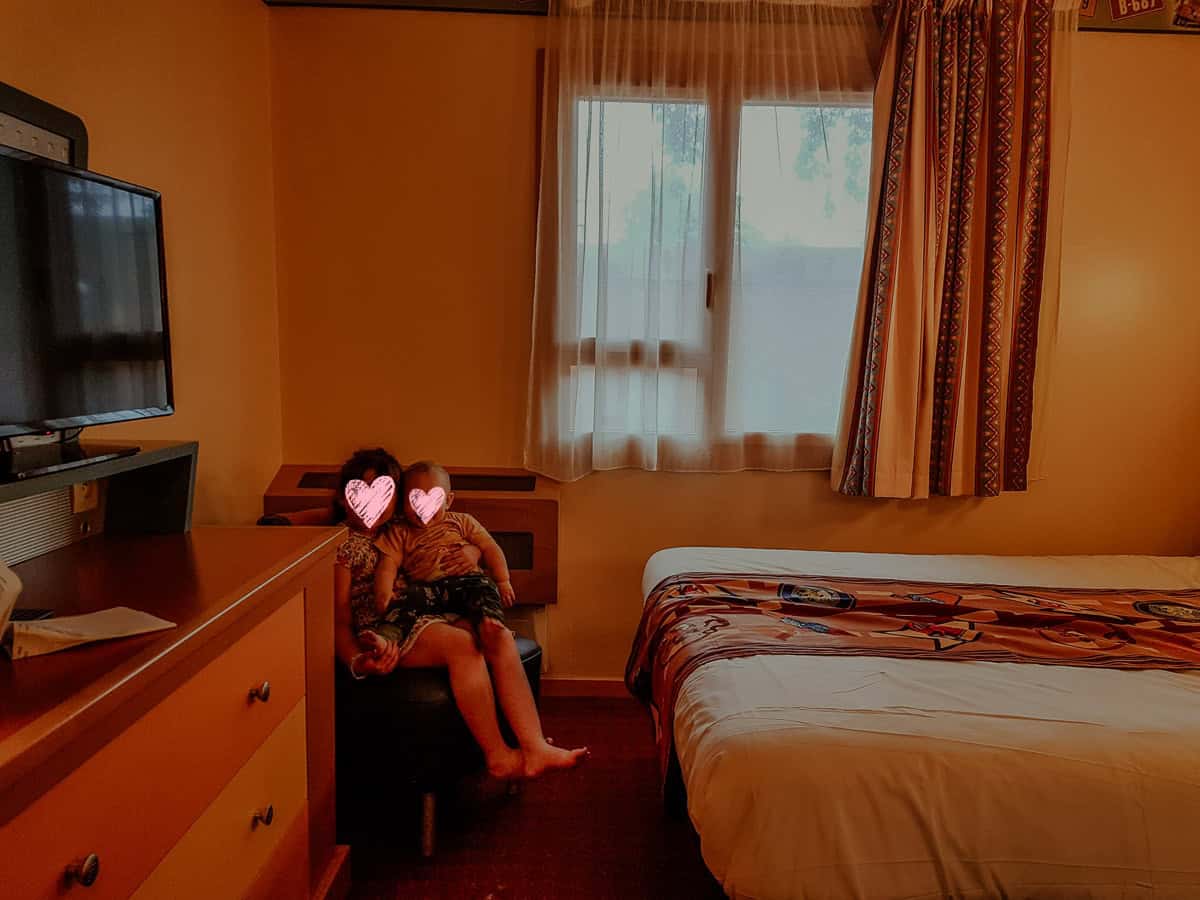 Norah sits on a dark footstool, holding Oscar on her lap beside a large dresser.