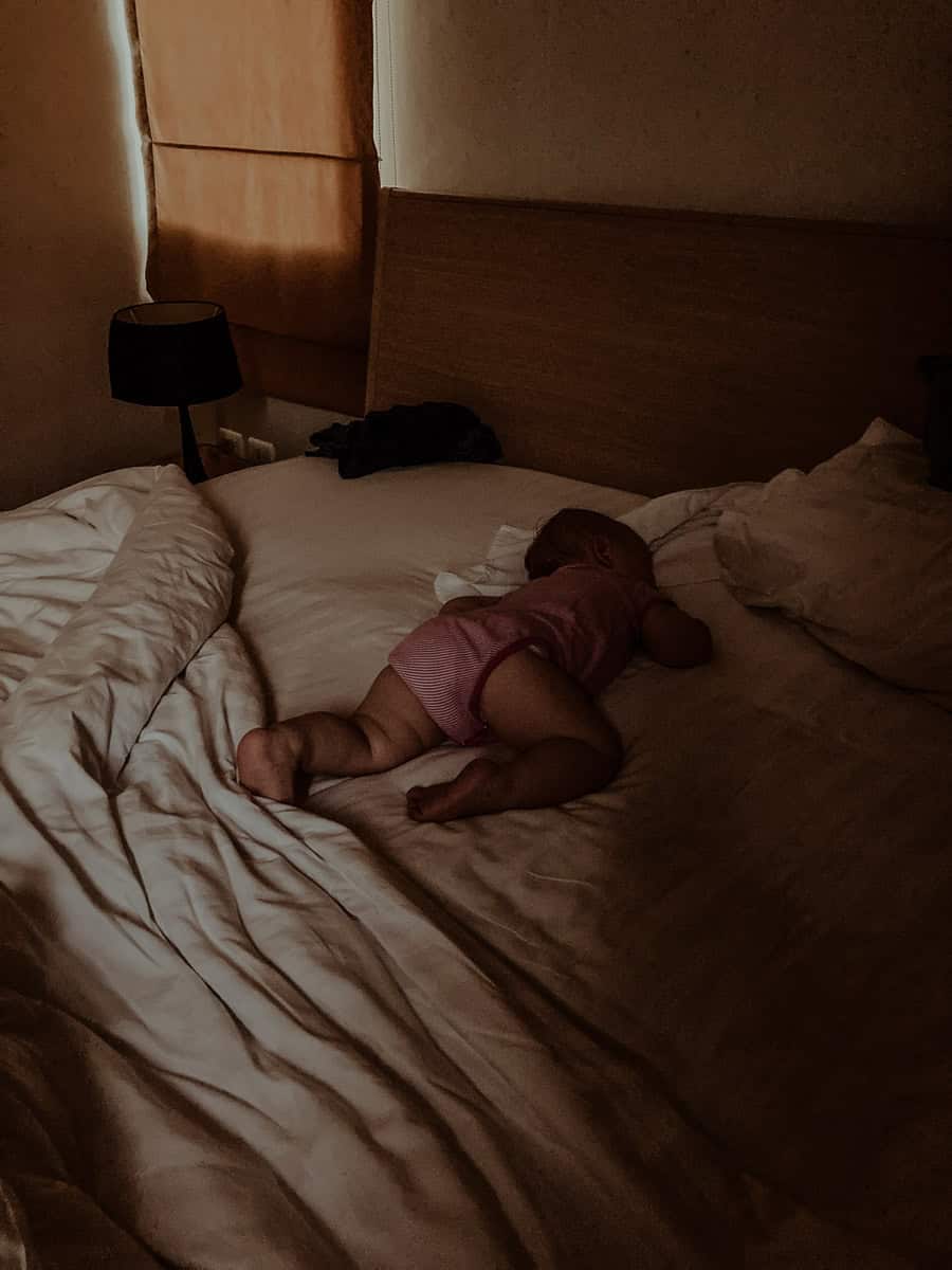 A high-angle view of a baby sleeping on its stomach at the center of a large bed.