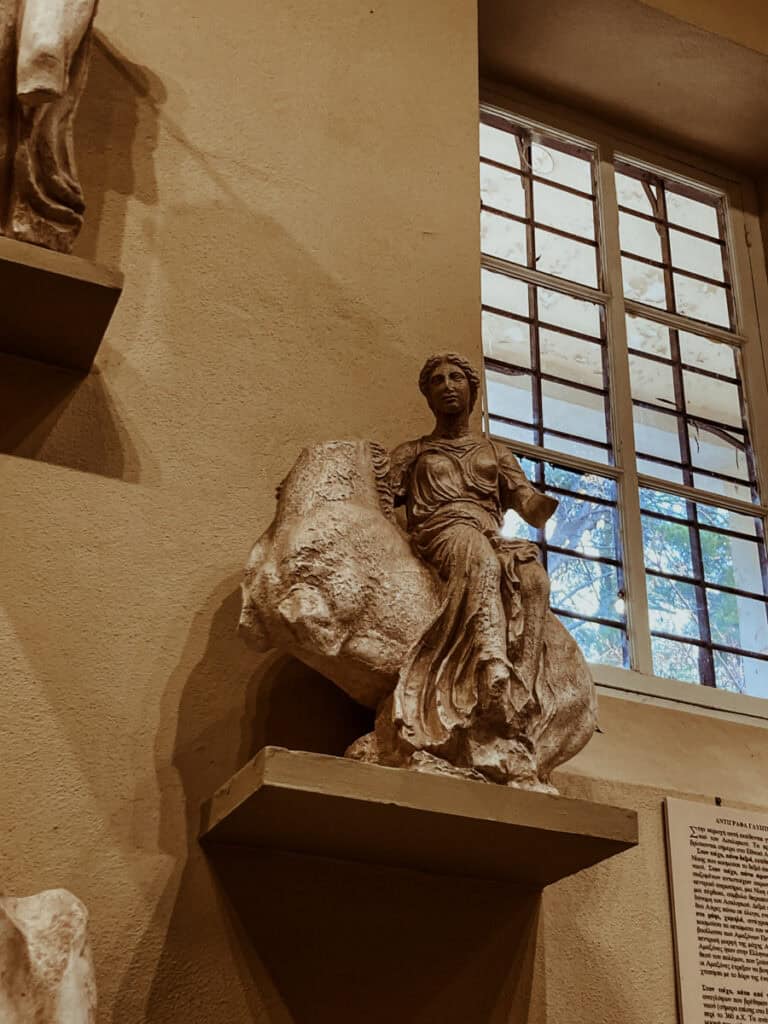 Weathered marble sculpture of a female figure riding a horse, displayed in a museum with visible damage and missing parts.