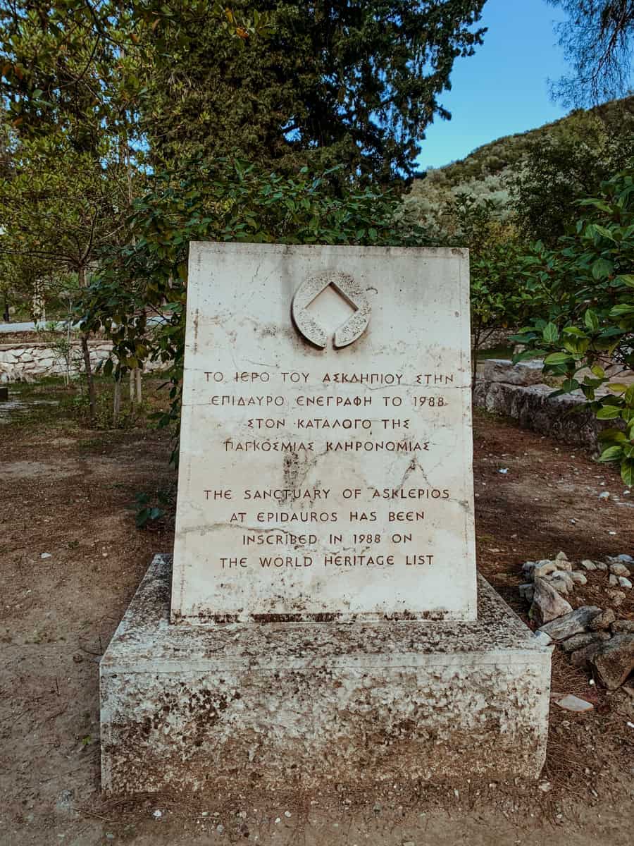 A stone UNESCO World Heritage monument plaque with text in Greek and English marking the Sanctuary of Asklepios at Epidaurus.