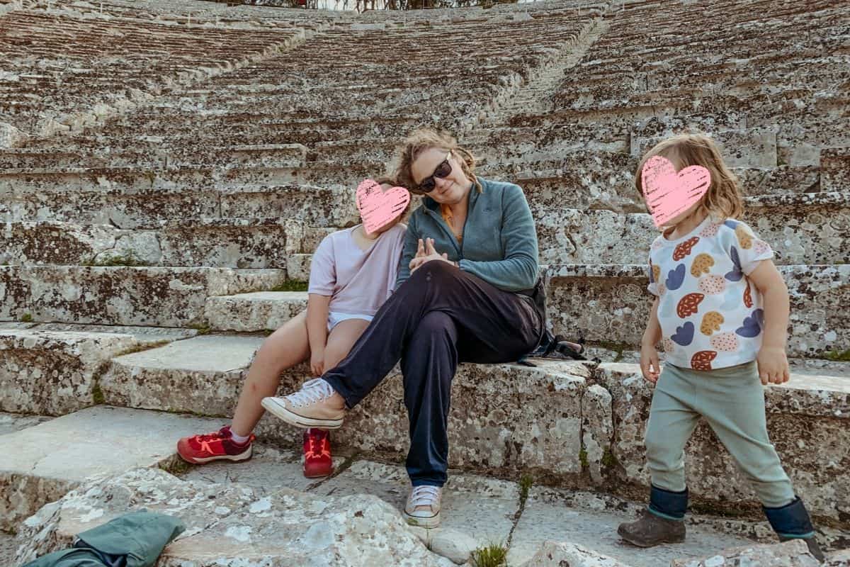 Kath with Norah and Oscar sitting on the bottom step of the Ancient Theatre of Epidaurus.