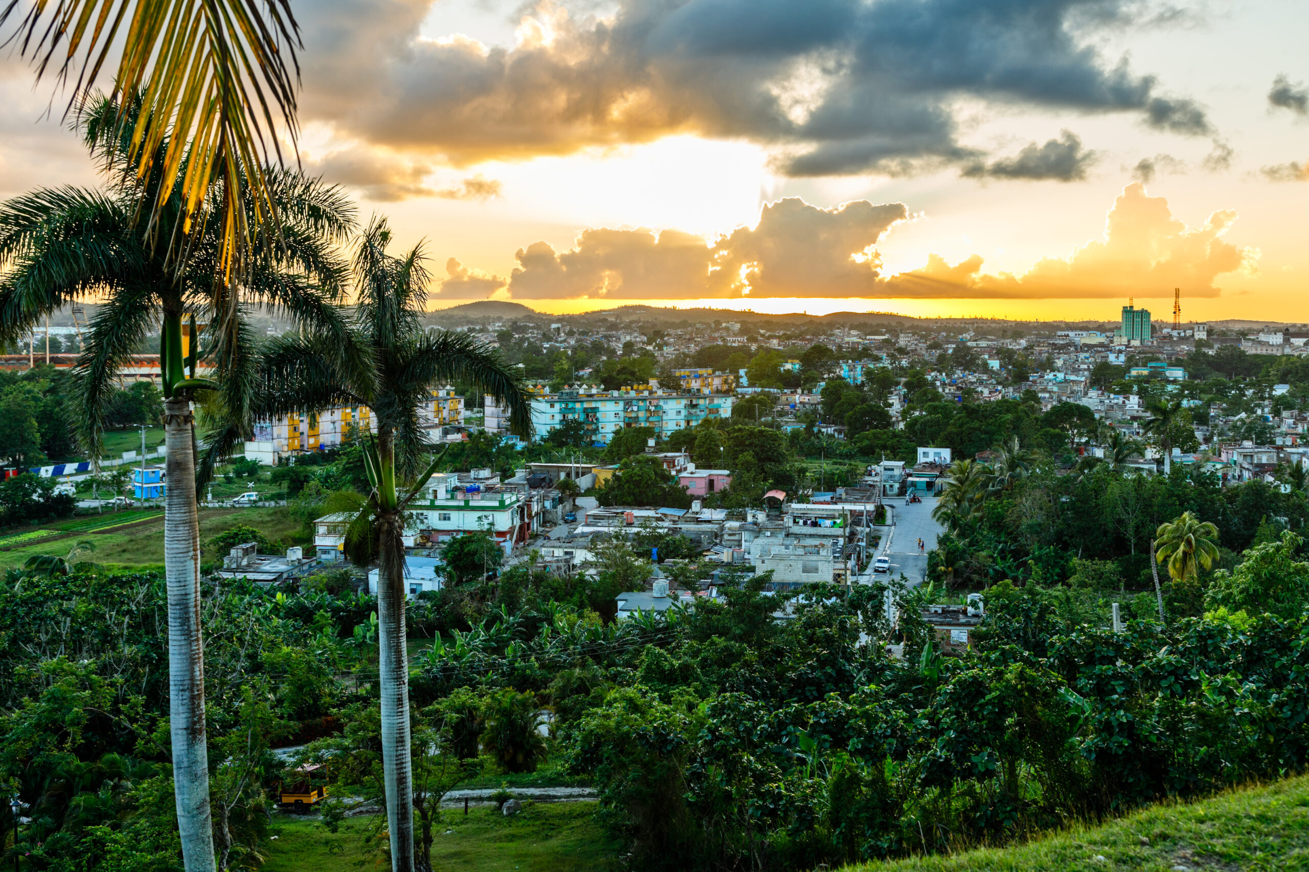 A sunset view over Santa Clara, Cuba, with palm trees and green foliage.