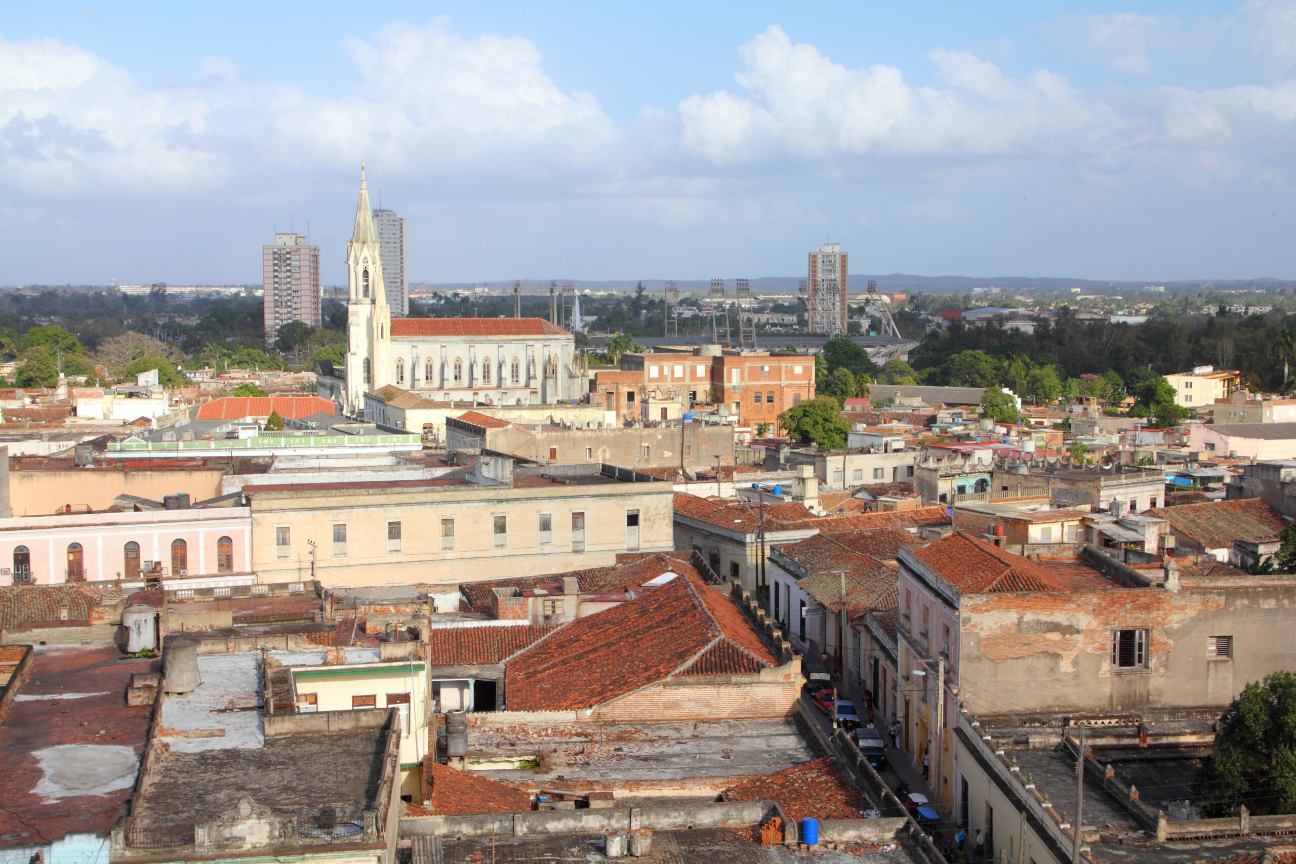 An elevated view of Camagüey, Cuba, with a white church and tall steeple, terracotta roofs, and low-rise residential buildings.
